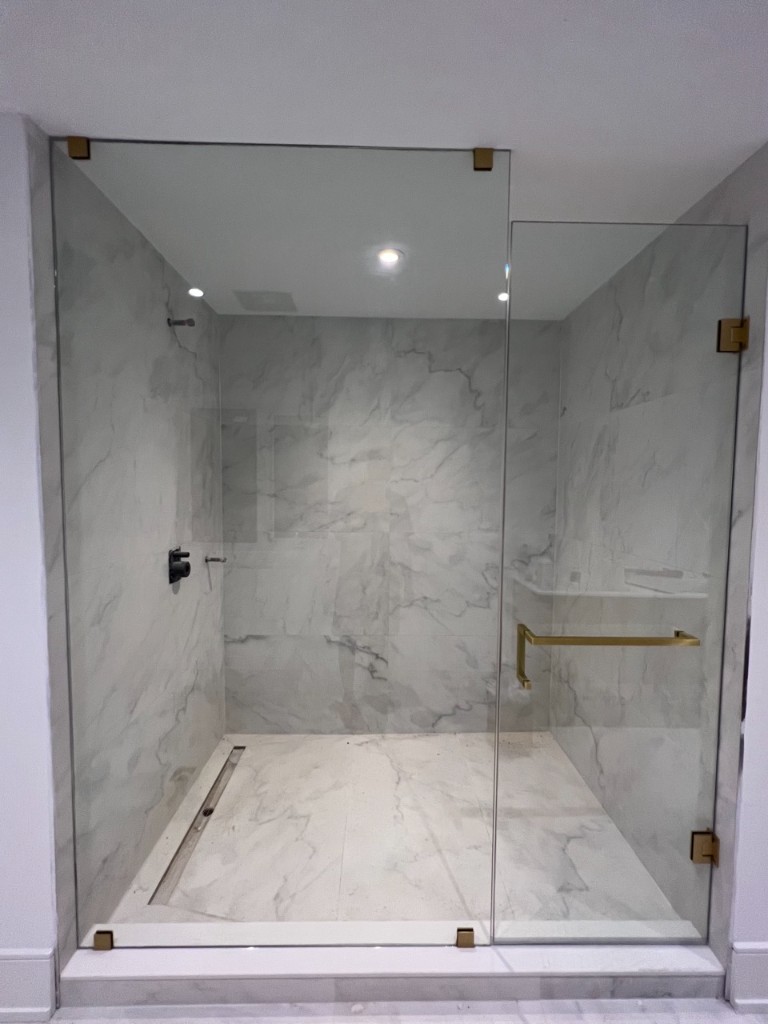 Frameless marble walk-in shower enclosure with gold hardware