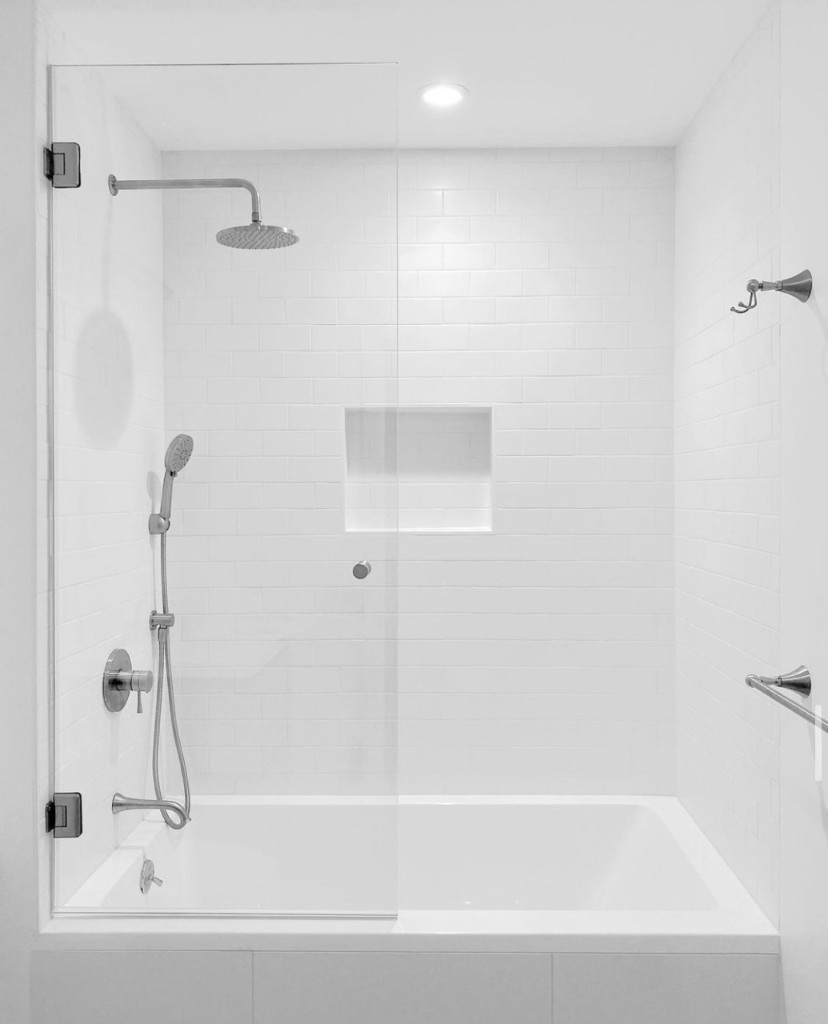 Frameless glass shower screen on a white subway-tile tub